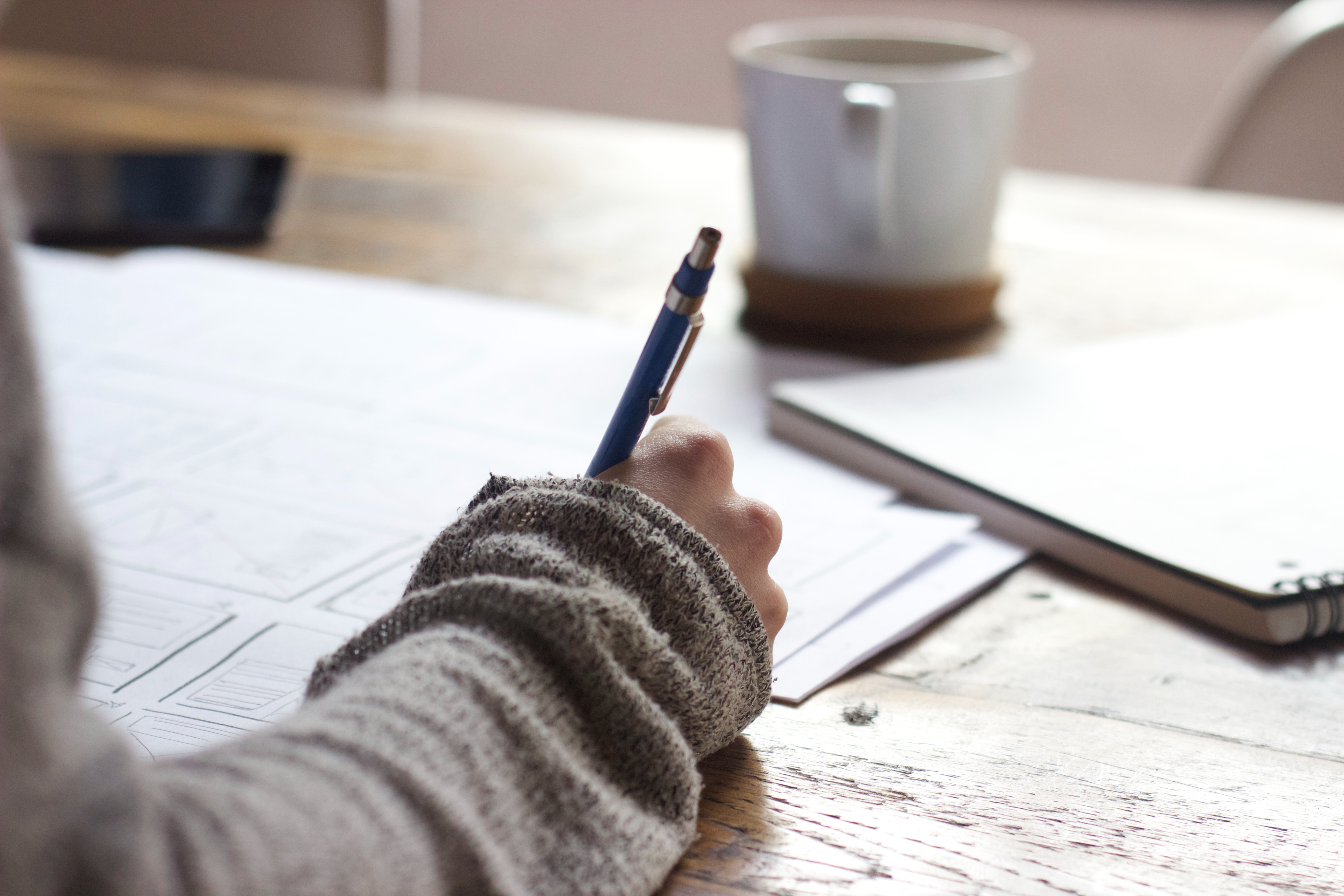 image of a hand writing on paper at a desk